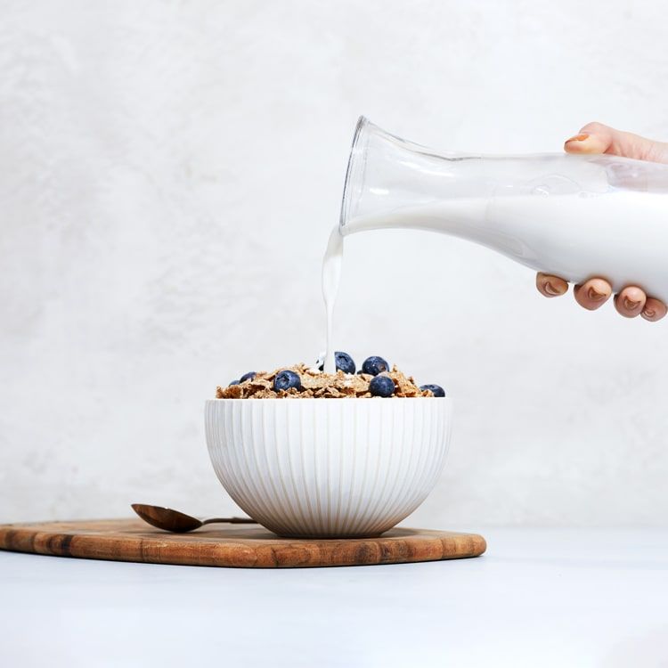 oat milk being poured in a bowl of cereal