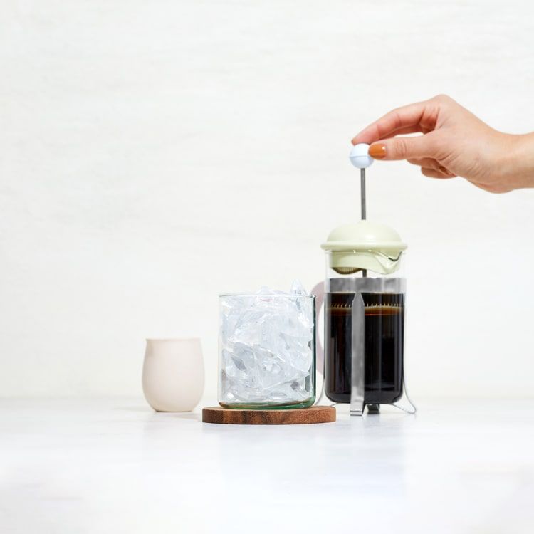 a glass of ice with a coffee press being pressed behind it